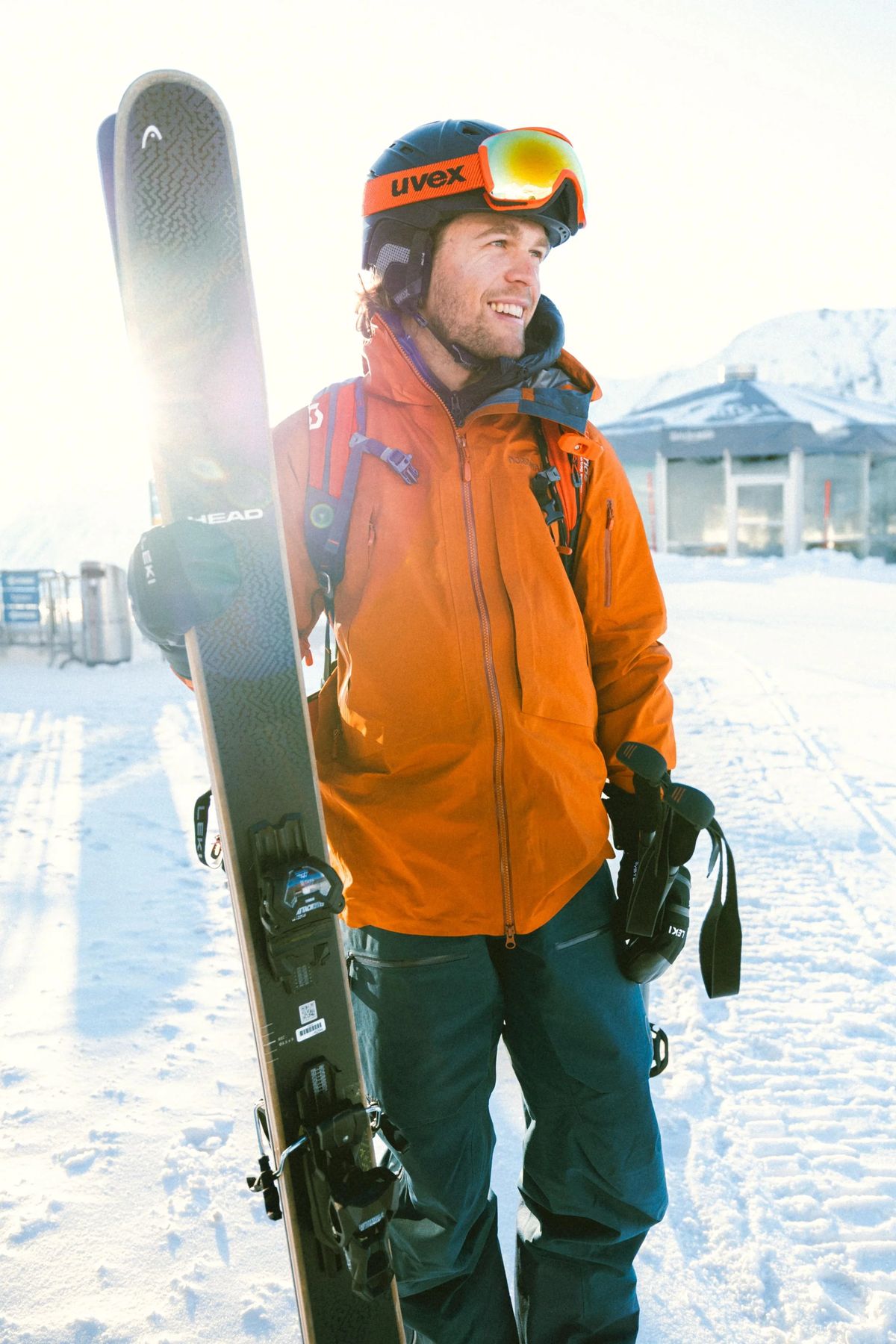 Lucas Kampf in oranger Skijacke mit Ski über der Schulter im Schnee