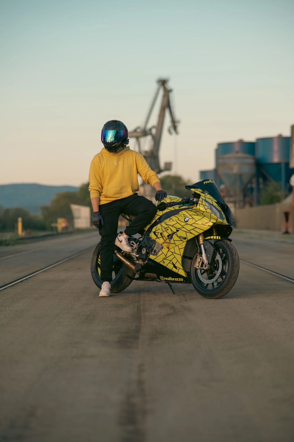 Fahrer in gelber Jacke neben einer BMW RR vor Hafenkränen